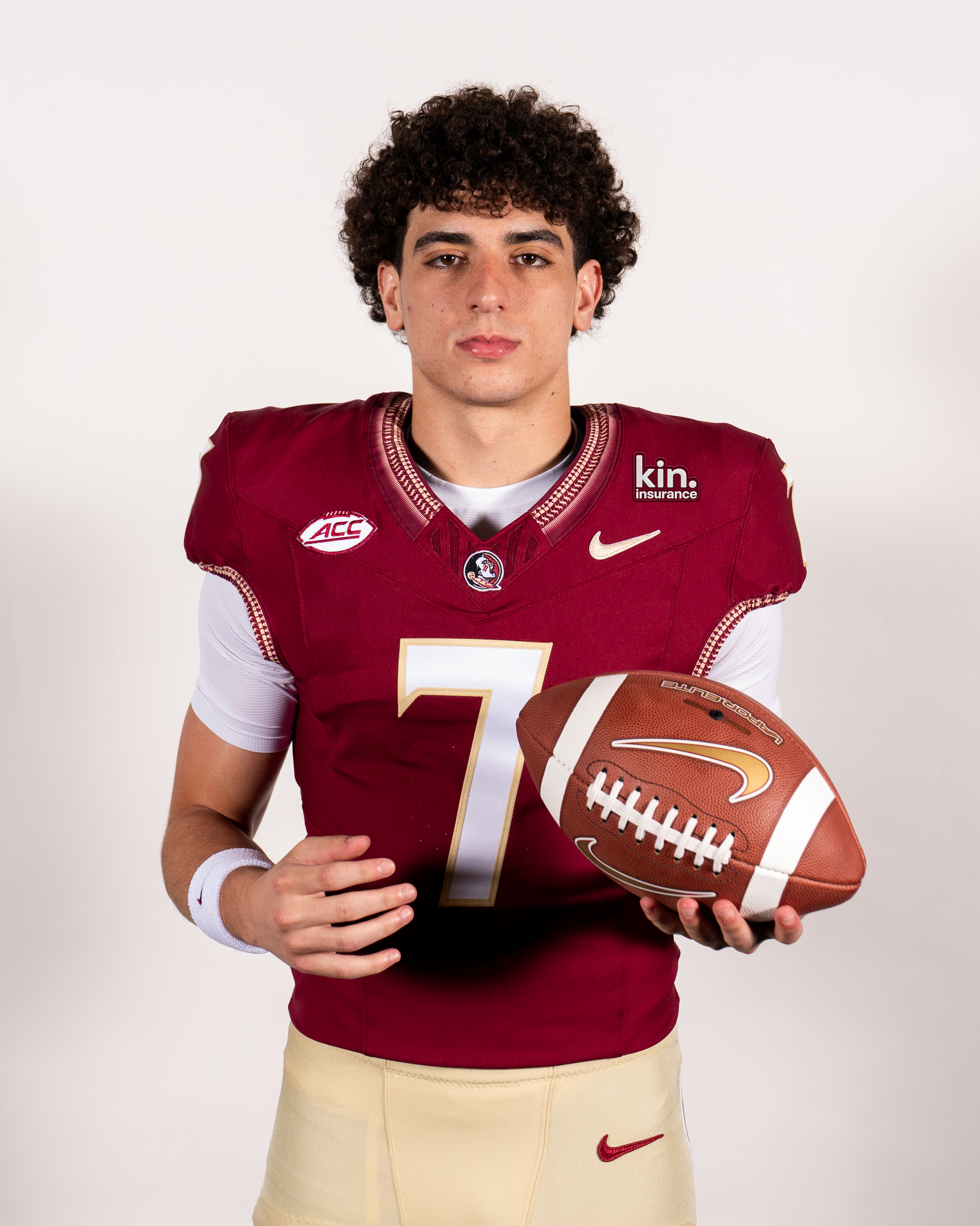 Florida State football player holding a football, wearing a jersey with the Kin insurance patch
