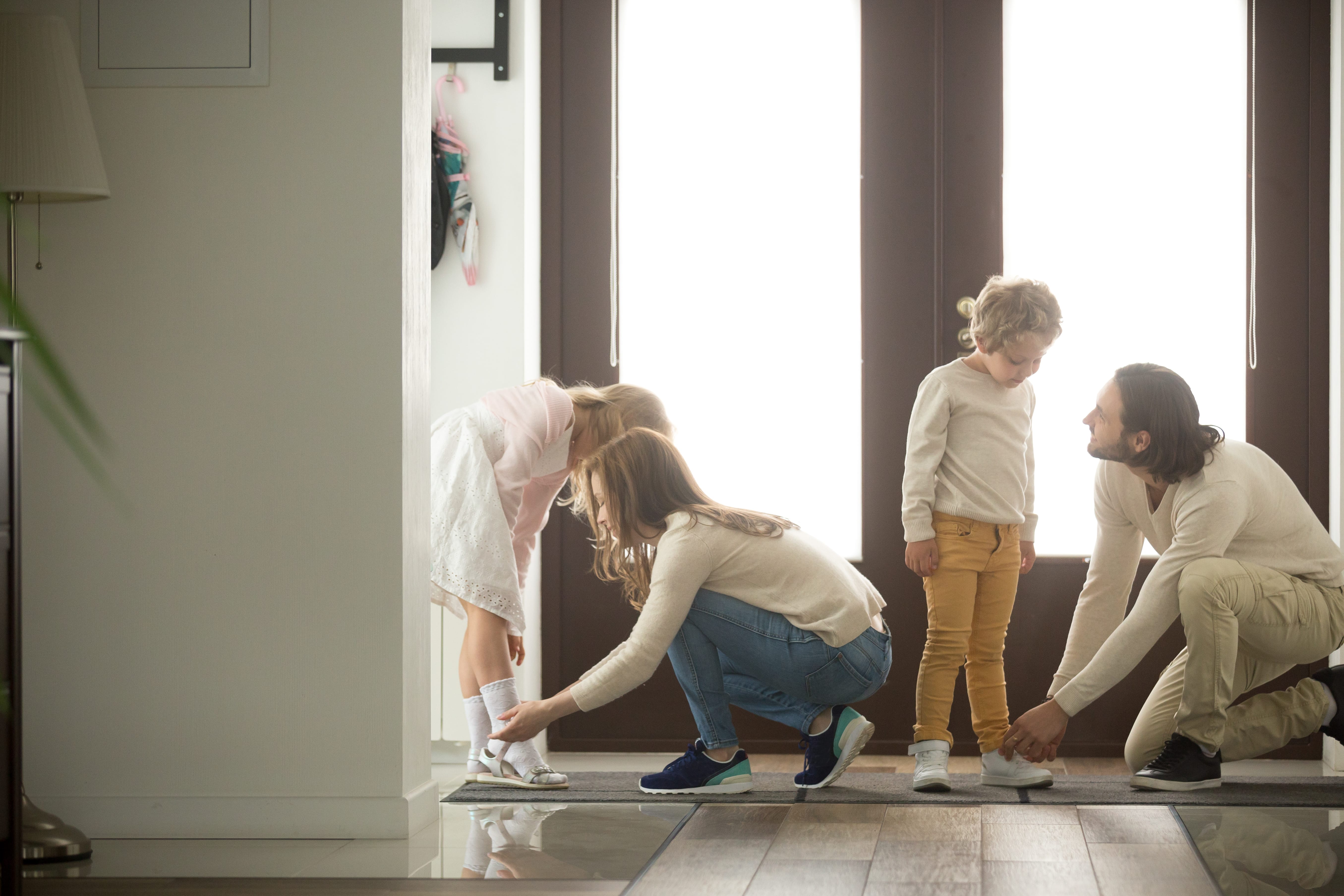 parents lacing up their children's shoes by the front door of a home