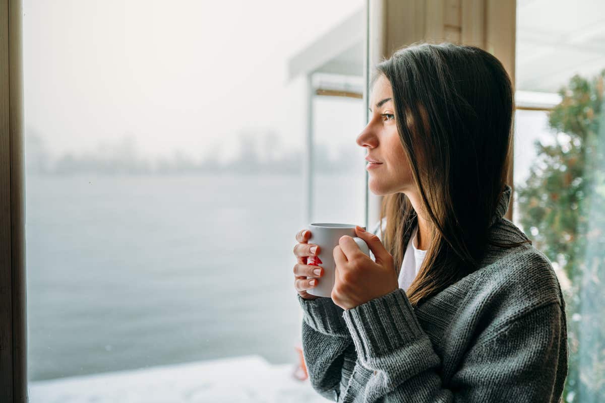 A woman looks out a window, drinking coffee