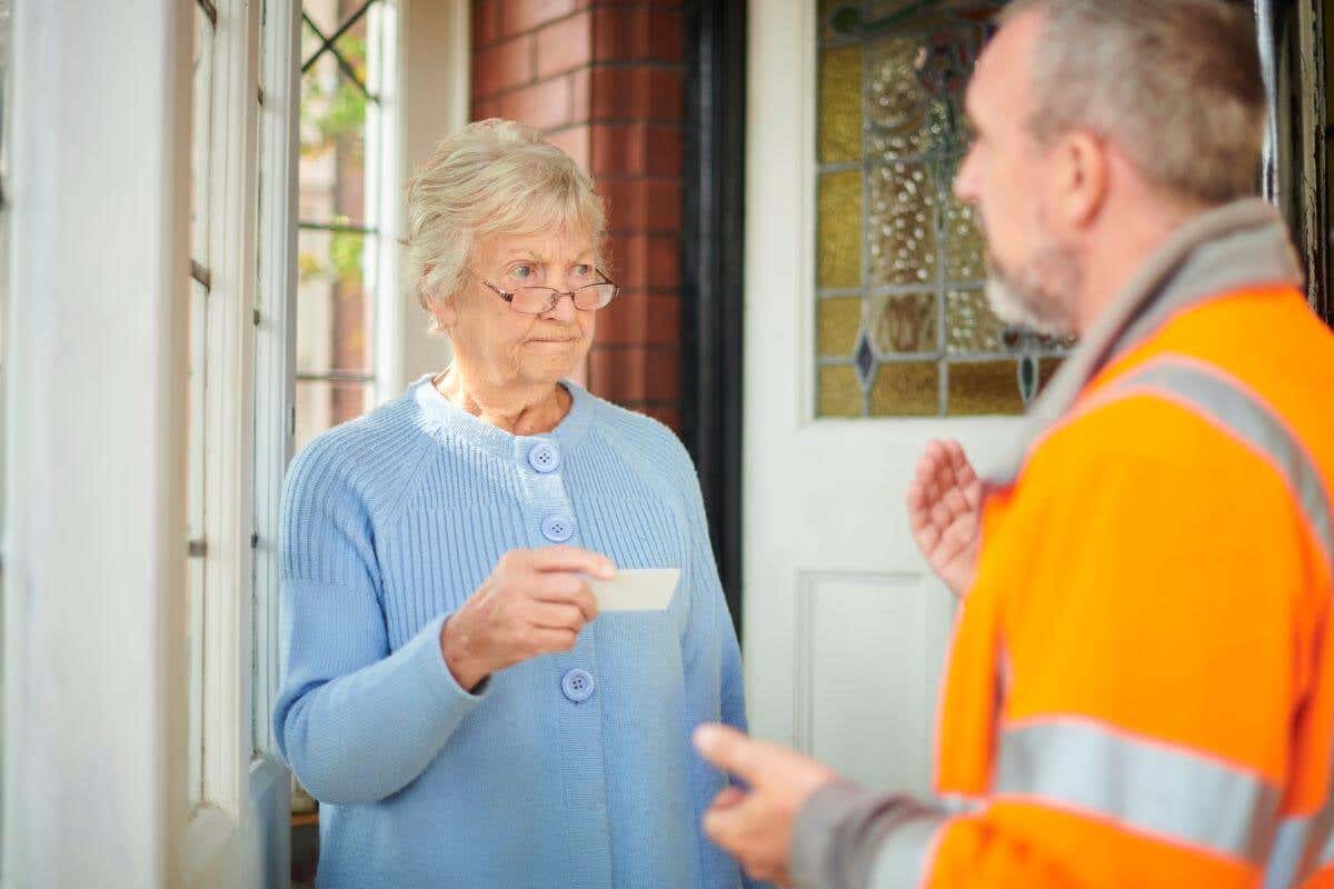 An older woman hold a contractor's card while looking at him skeptically