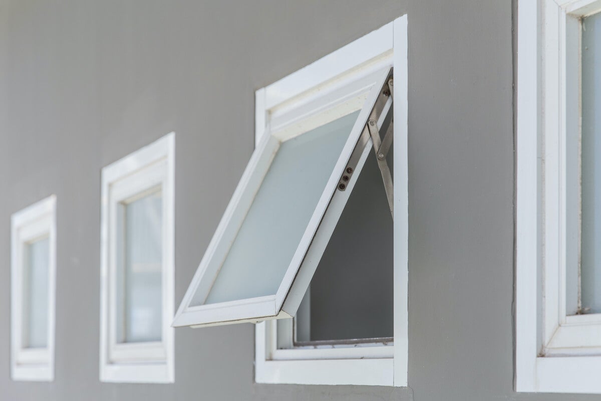 Exterior of a gray house with a close-up of an open, white awning window