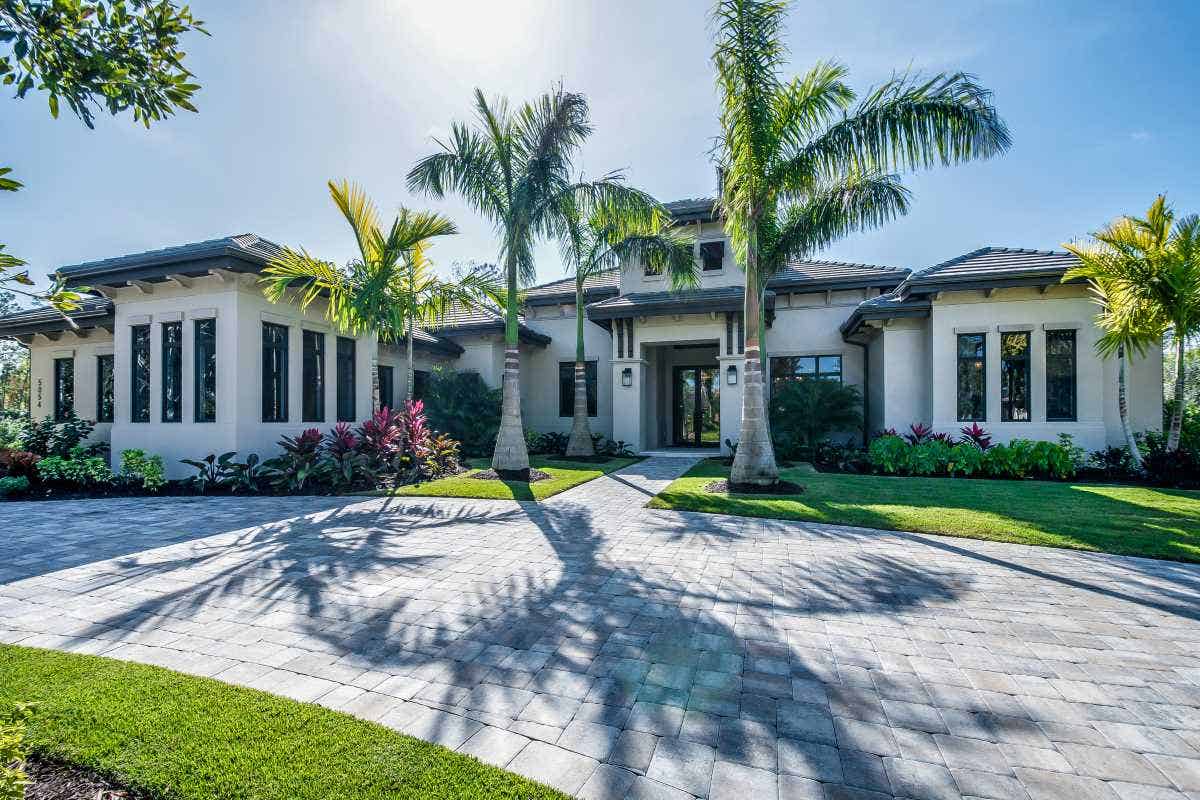 A stunning home with a grand entrance, palm trees, and a stone circle driveway