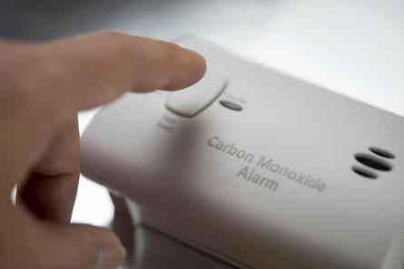 A finger pressing the test button on a carbon monoxide detector