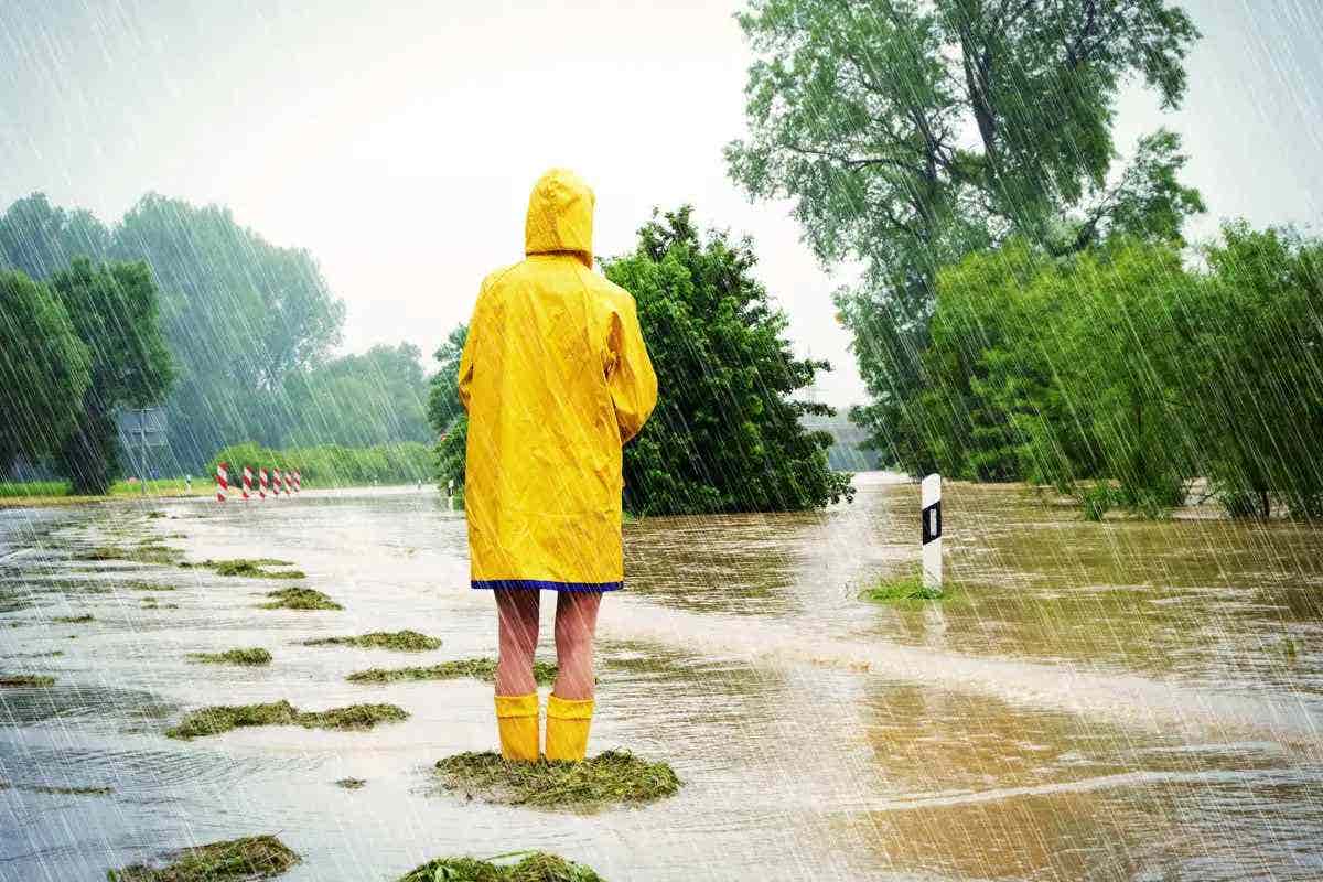 A person in a yellow raincoat looks upon a flooded street as it rains