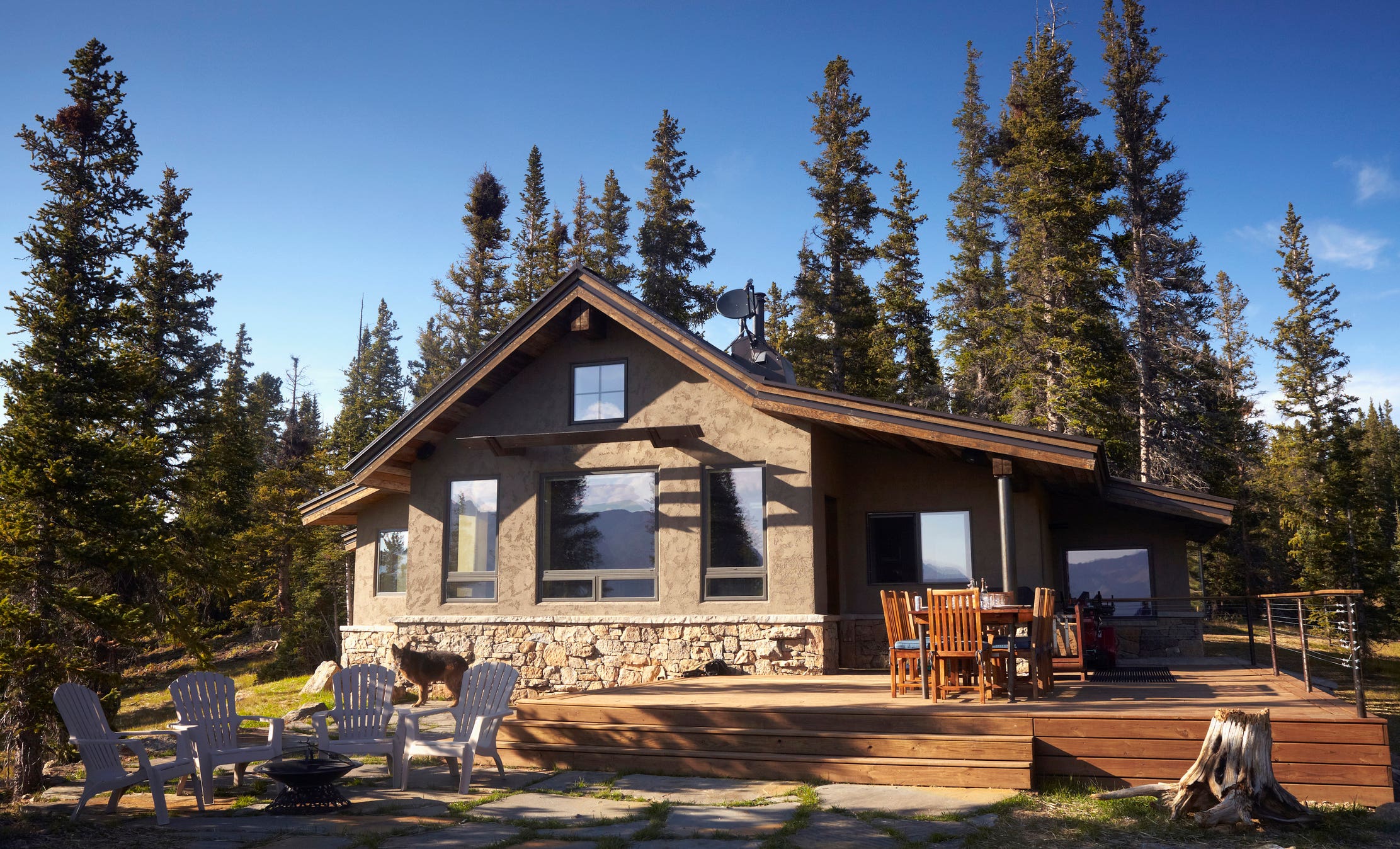 House among evergreen trees with large deck and outdoor living space.