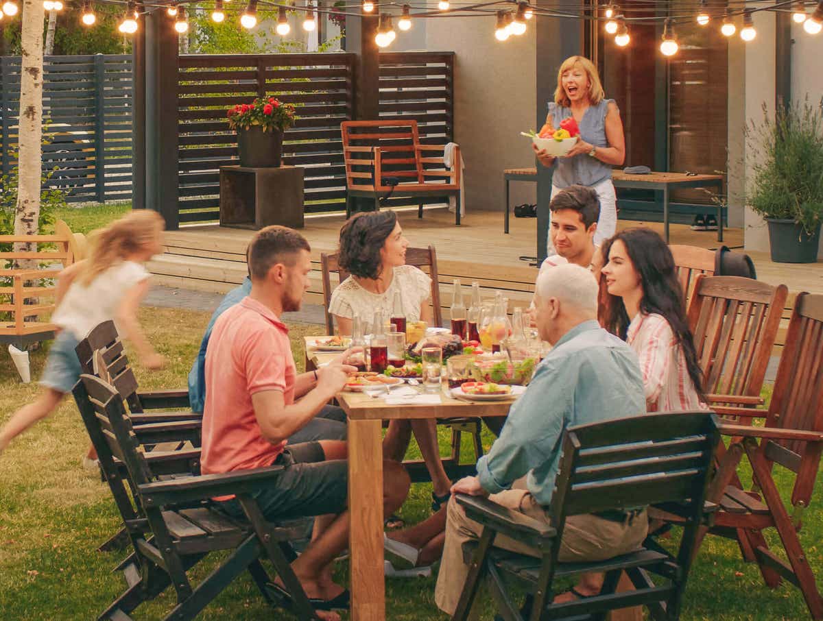 A multigenerational family gather for a meal in their backyard