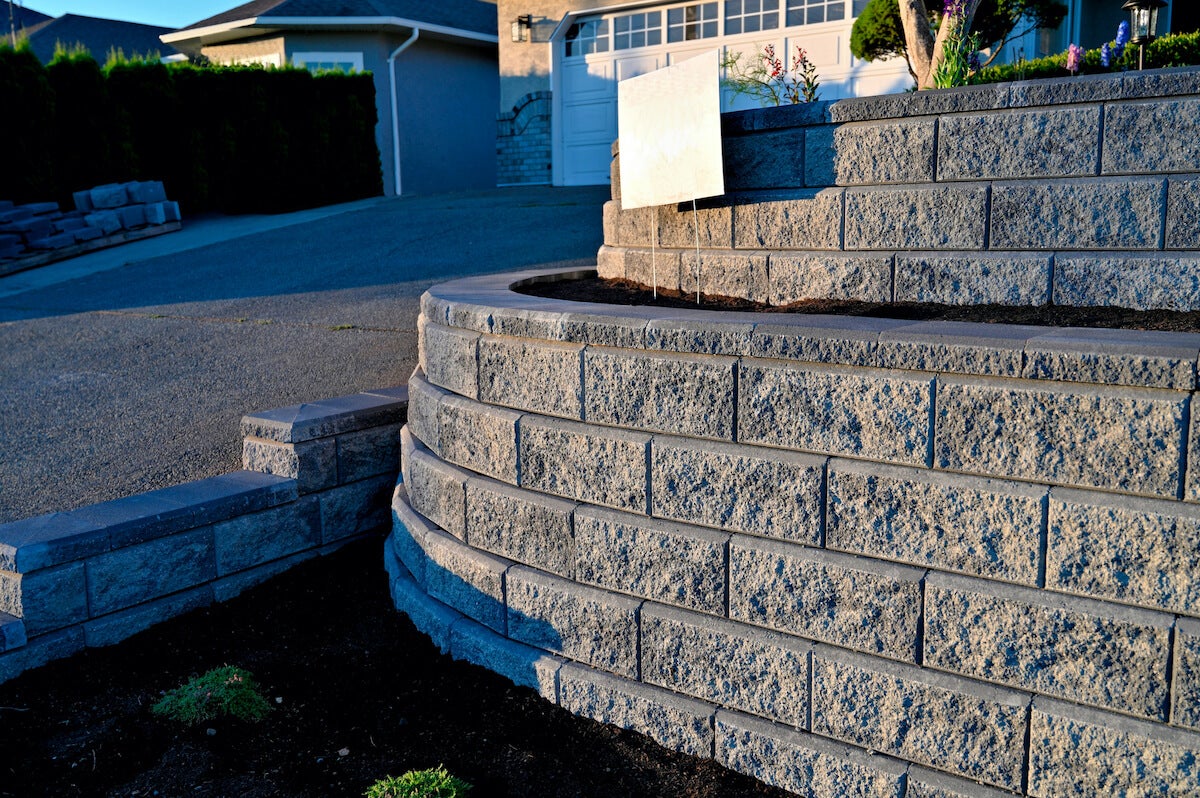 A two-tiered retaining wall made of stone next to an asphalt driveway