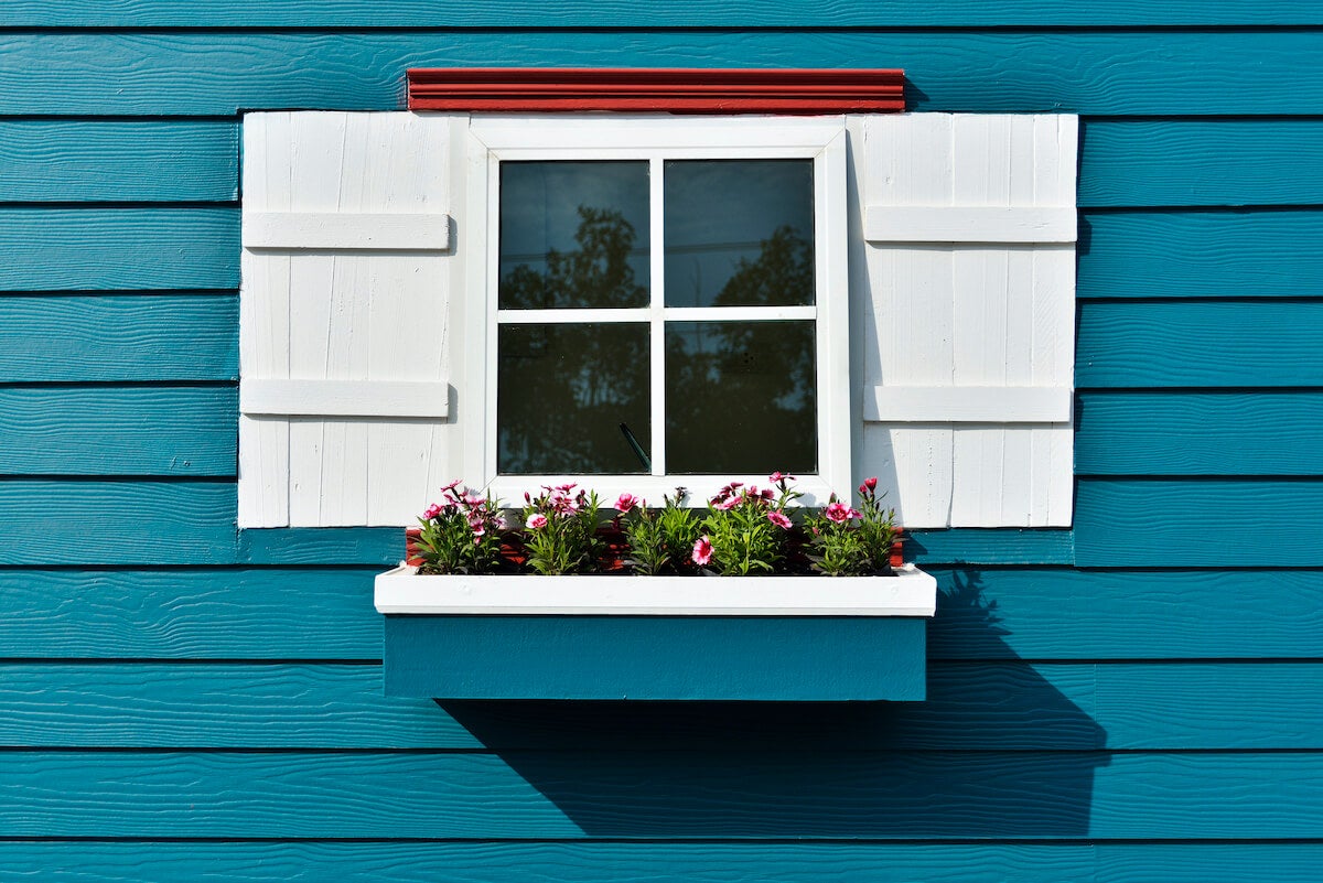 Closeup of white shutters and window box with flowers on a bright blue house