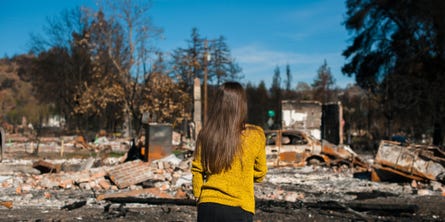 A woman stands with her back to the camera looking at a demolished home
