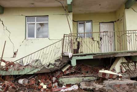 A home with cracks in its walks surrounded by rubble