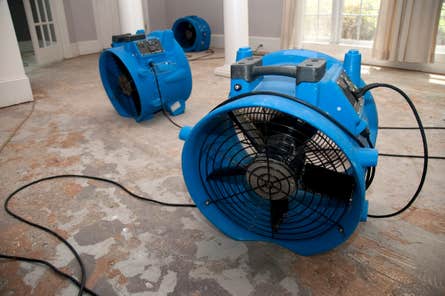 Interior of a home with the flooring ripped off and three large, blue industrial dehumidifiers 