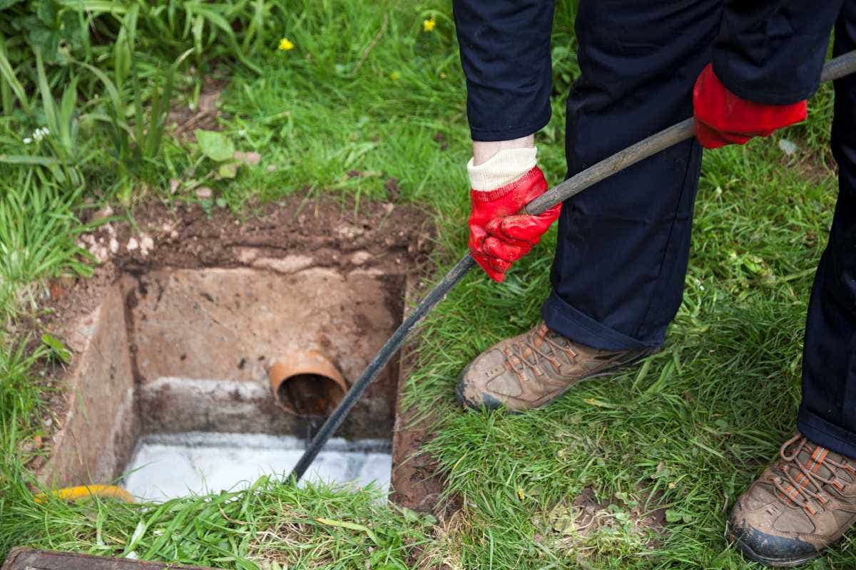 A drain being cleared by worker in navy overalls