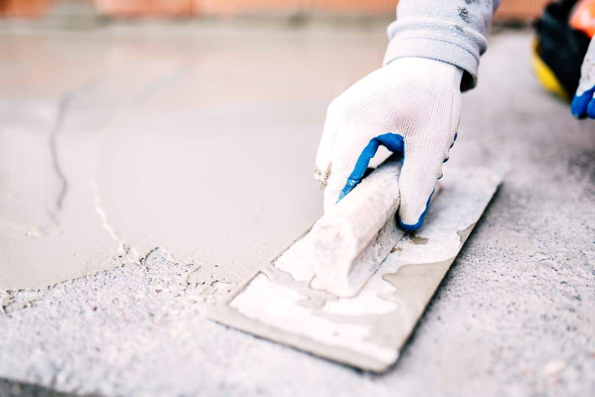 A worker's gloved hand laying sealant for waterproofing cement