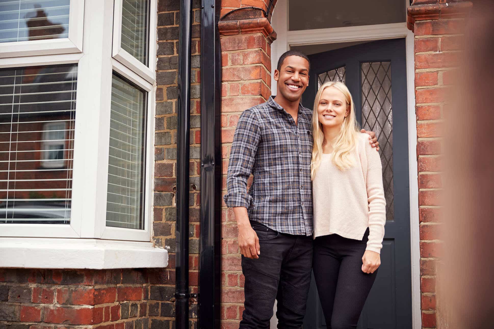 A couple stands on the front porch of their brick home