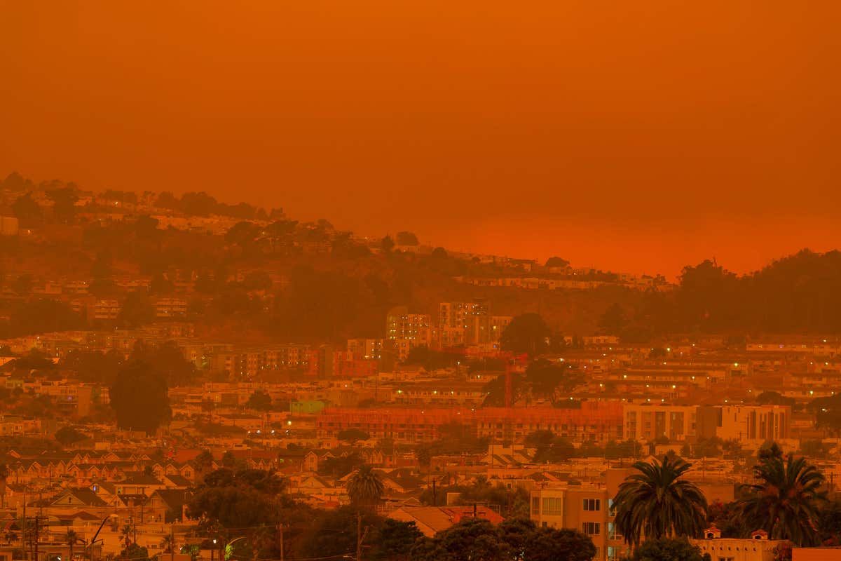 A red sky caused by wildfire over a town near a mountain and forest