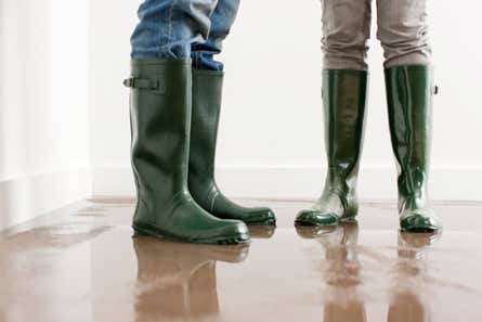 Close-up of two people's feet wearing rain boots and surrounded by water