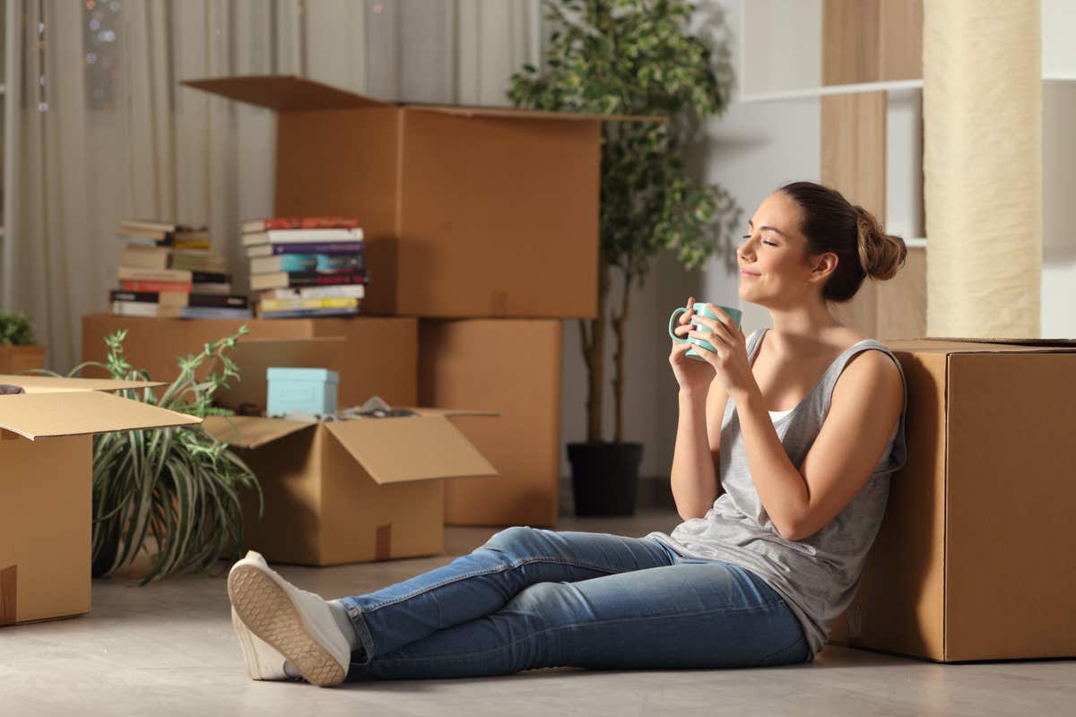 a smiling woman sits on the floor surrounded by moving boxes