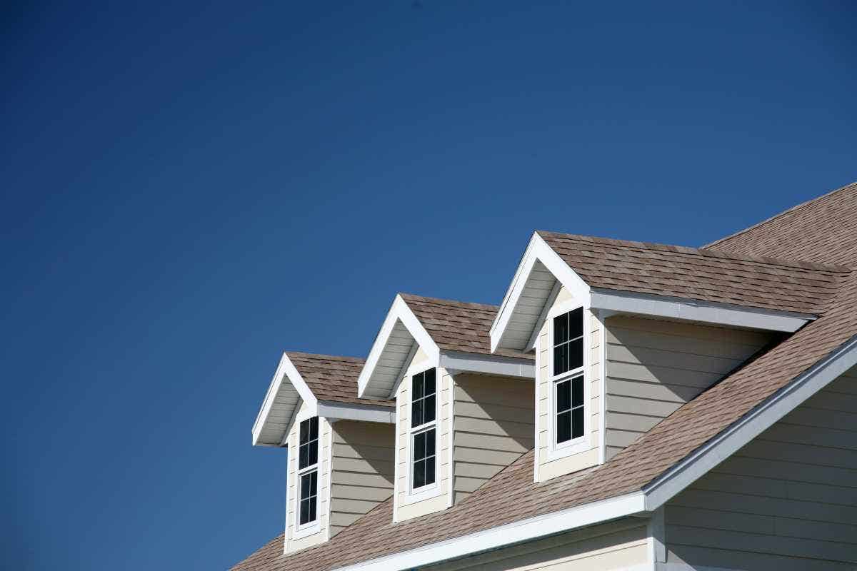A roof with three dormers against a bright blue sky