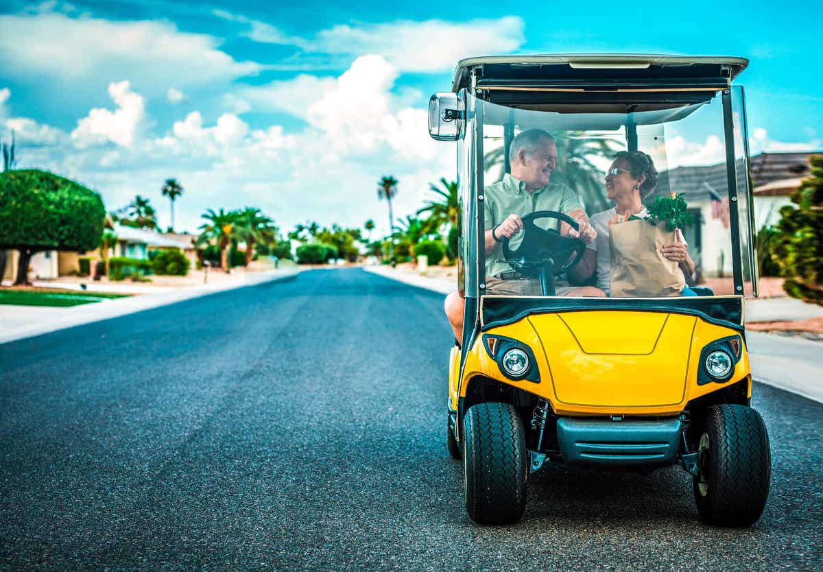 older man and woman in a yellow golf cart with palm trees in the background