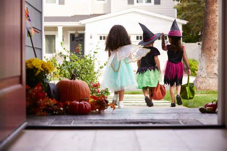The back of three children as the leave a home to go trick-or-treating