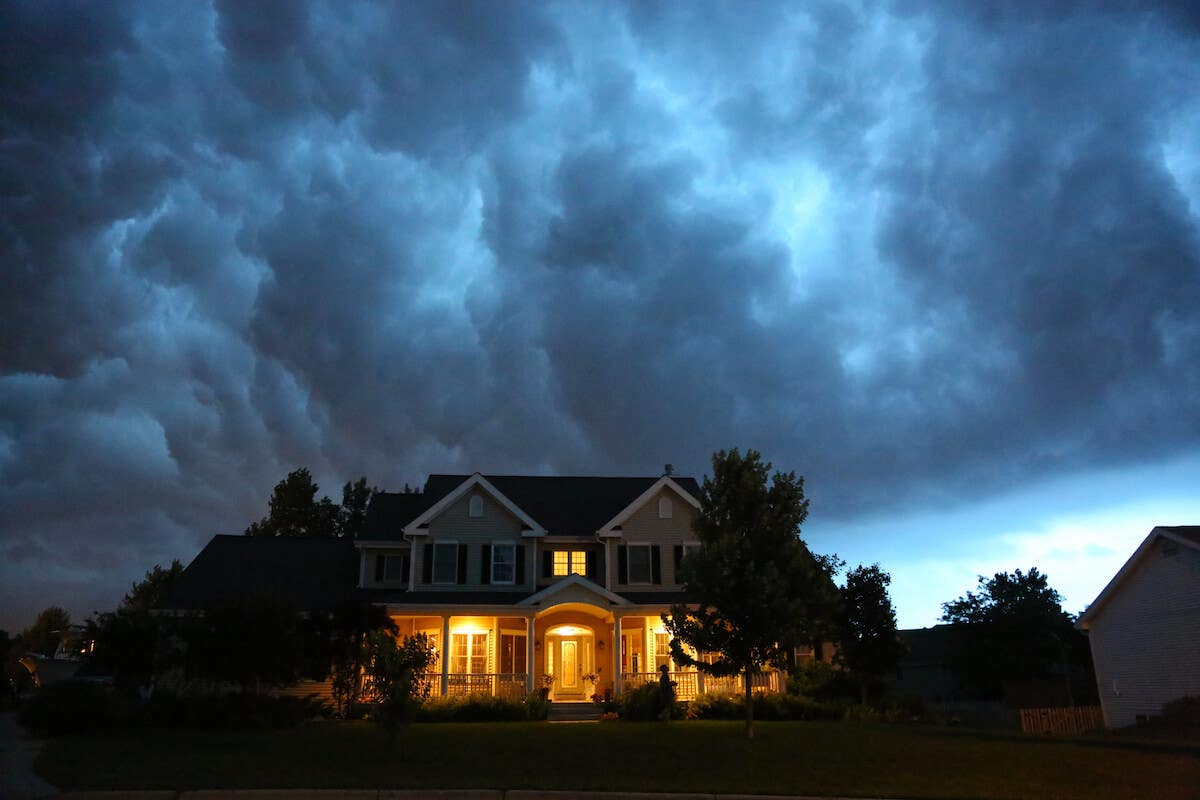 a two-story home with its porch lights on while storm clouds gather over a darkened sky overhead