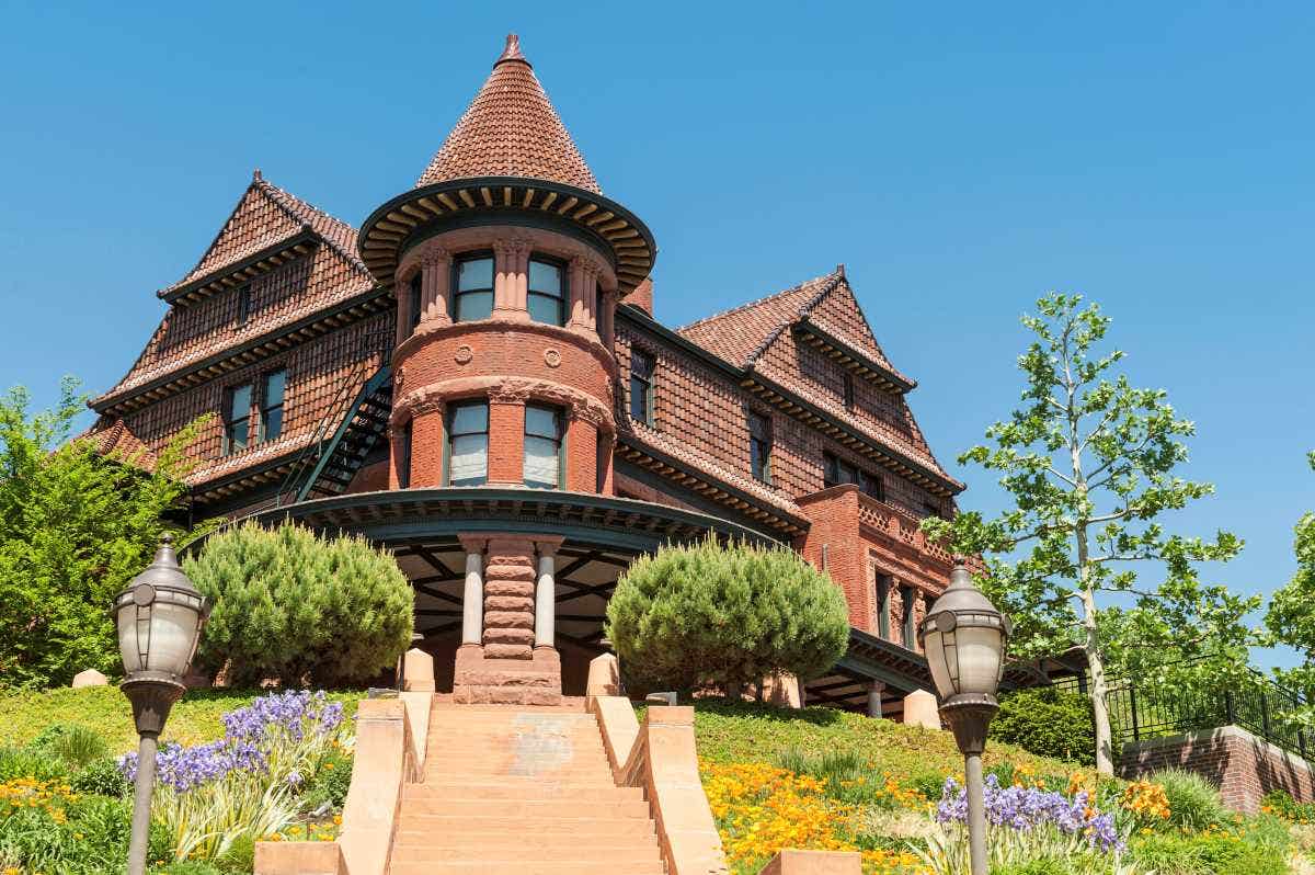A historic mansion with gothic turrets and colorful gardens against a clear blue sky