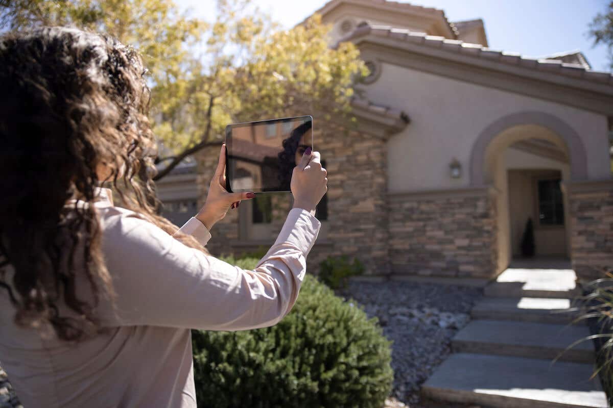 real estate agent taking photos of a brick home's exterior on a tablet