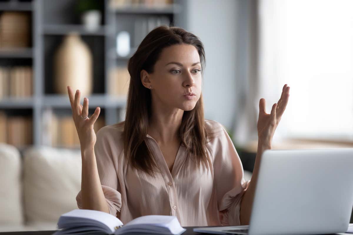 Frustrated young woman in front of a computer with her hands up in exasperation 