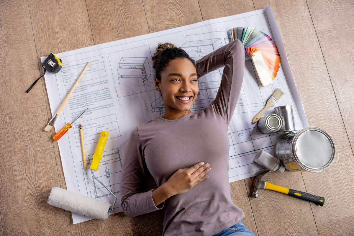 Happy woman lays on floor with her home remodel plans, paint samples, and tools