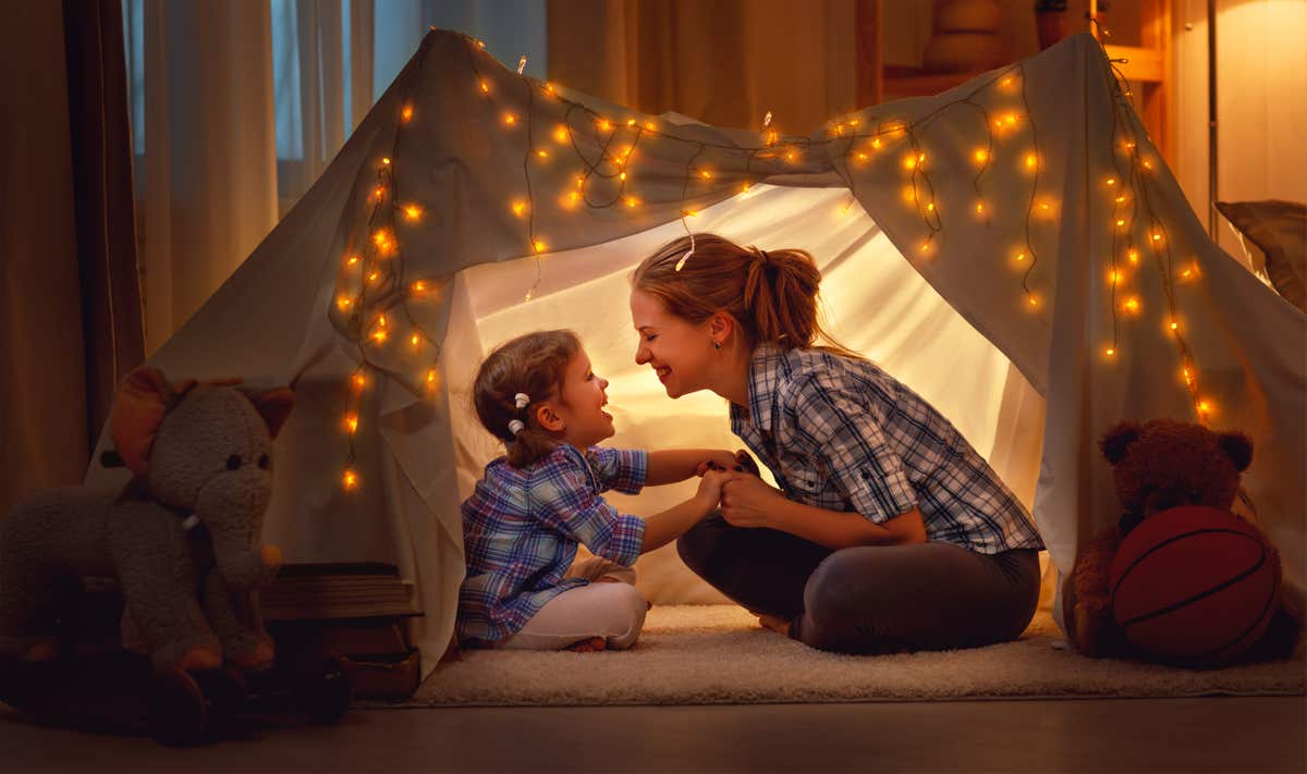 A small boy looks up at his mother as they play in a homemade fort in his bedroom