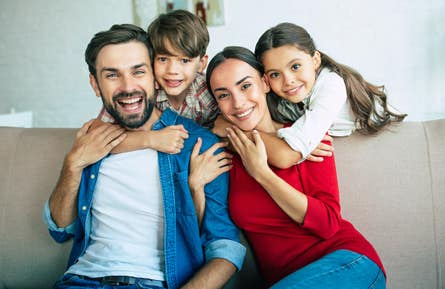 Husband and wife with their two children relax together at home smiling and hugging