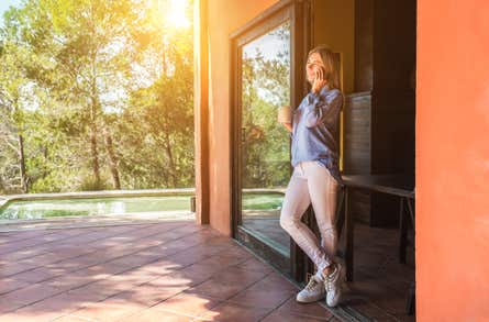 A female homeowner stands on her back patio, talking on her cell phone