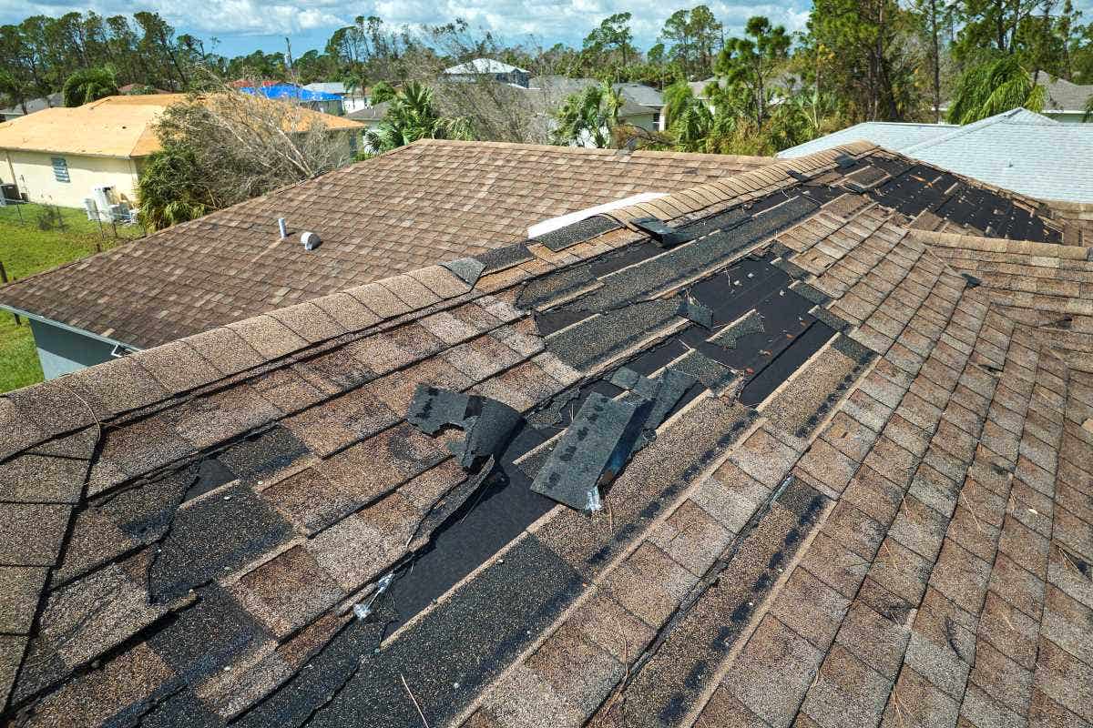 Home with a wind damaged roof with missing asphalt shingles after hurricane