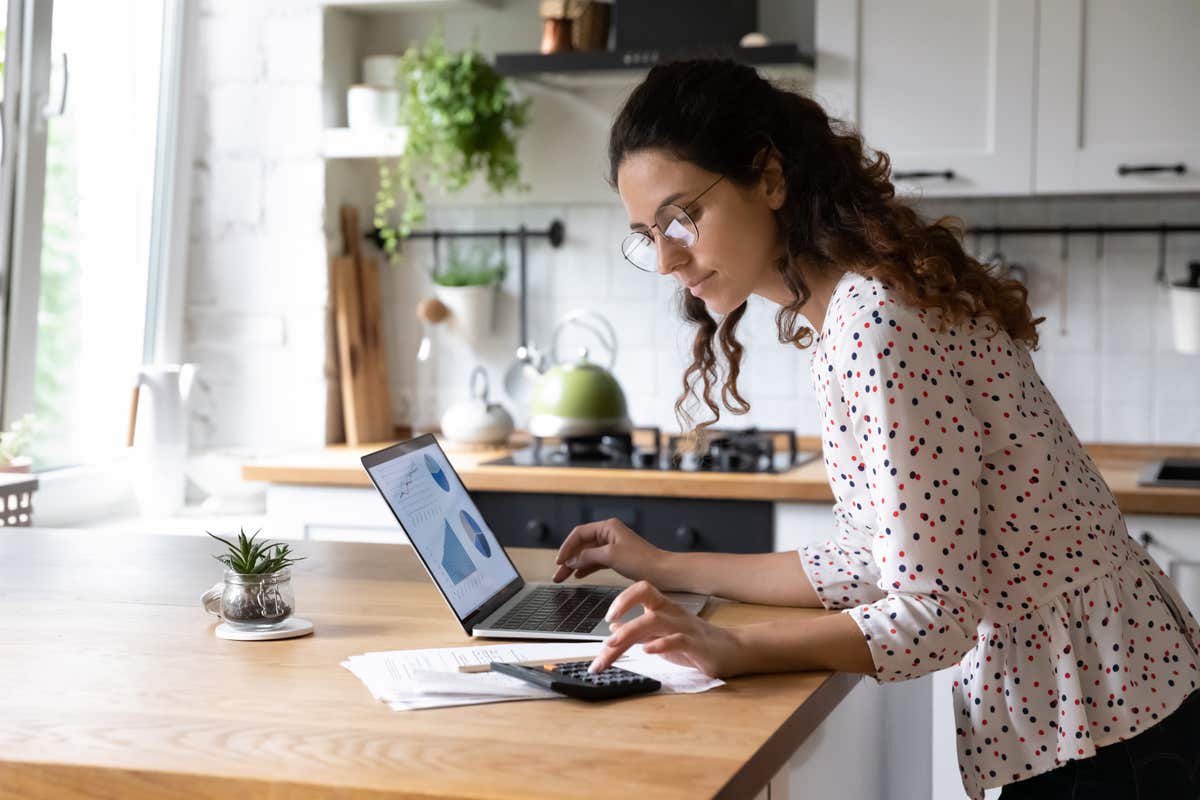 A woman stands at her kitchen idland, working on a laptop