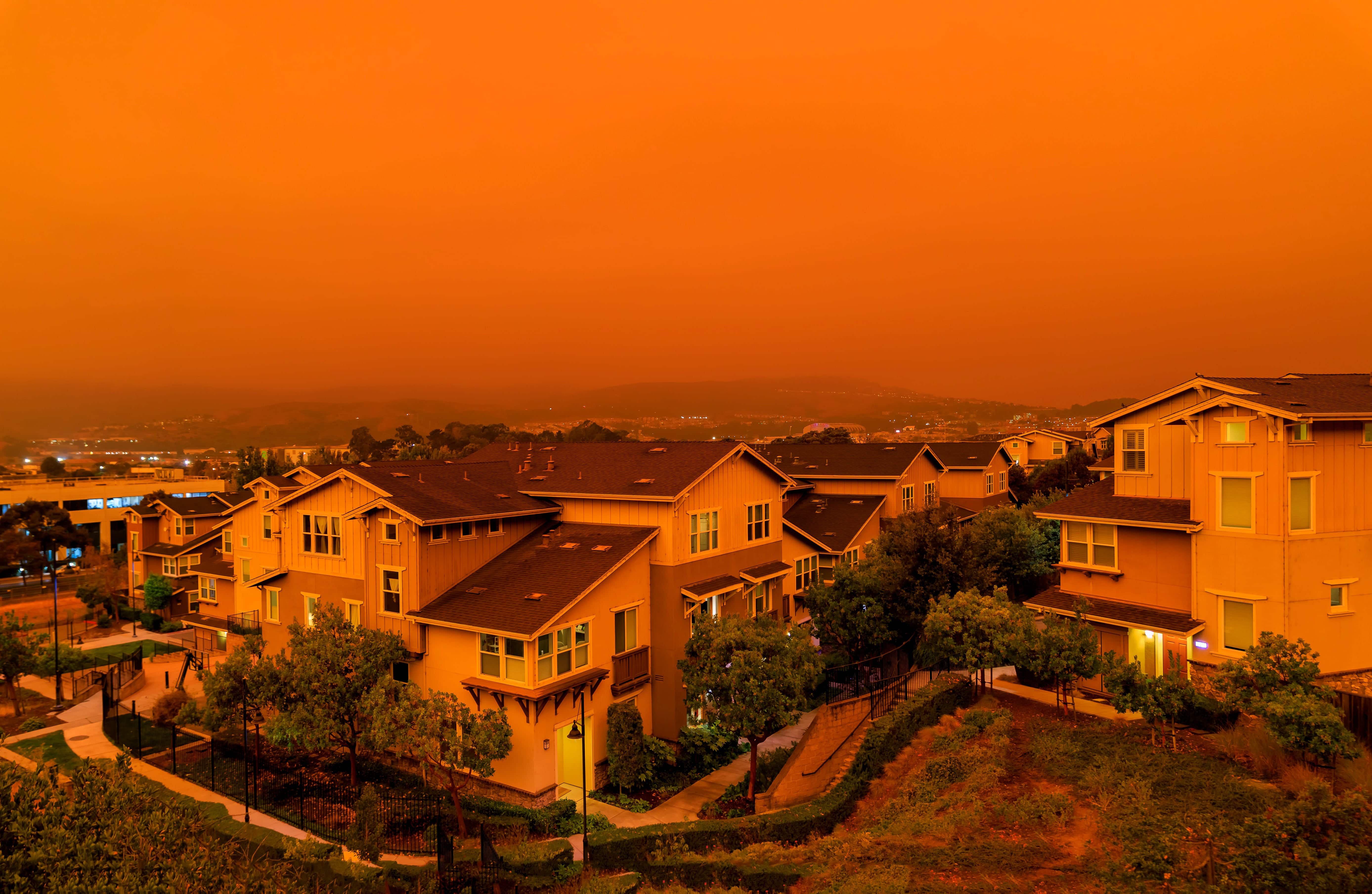 A residential area where red smog fills the sky from a nearby wildfire 