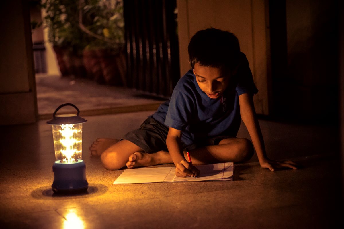 A young boy writes in a notebook by the light of an electric lantern during a power outage