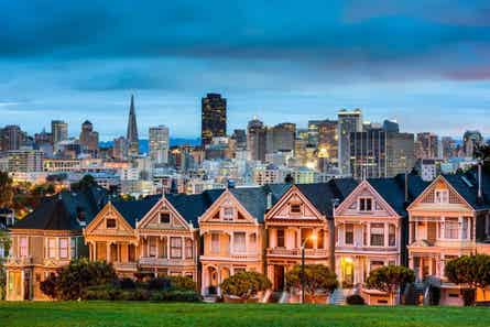 A row of Victorian homes with the San Francisco skyline in the background