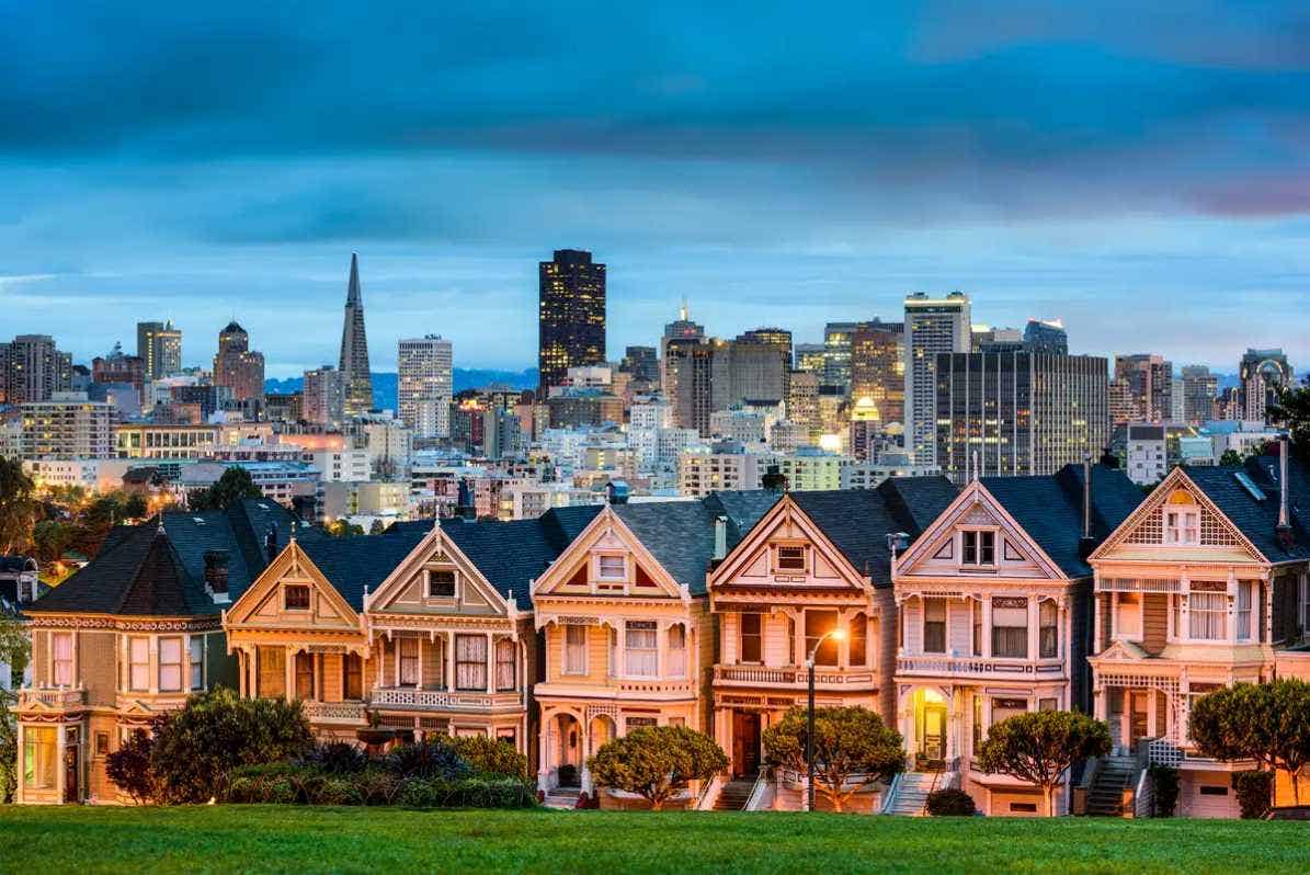 A row of Victorian homes with the San Francisco skyline in the background