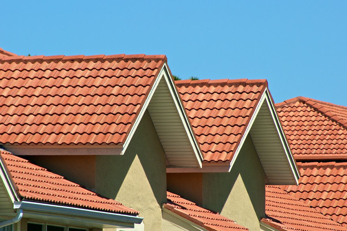 Several roof tops made of orange clay tile in front of a sunny blue sky