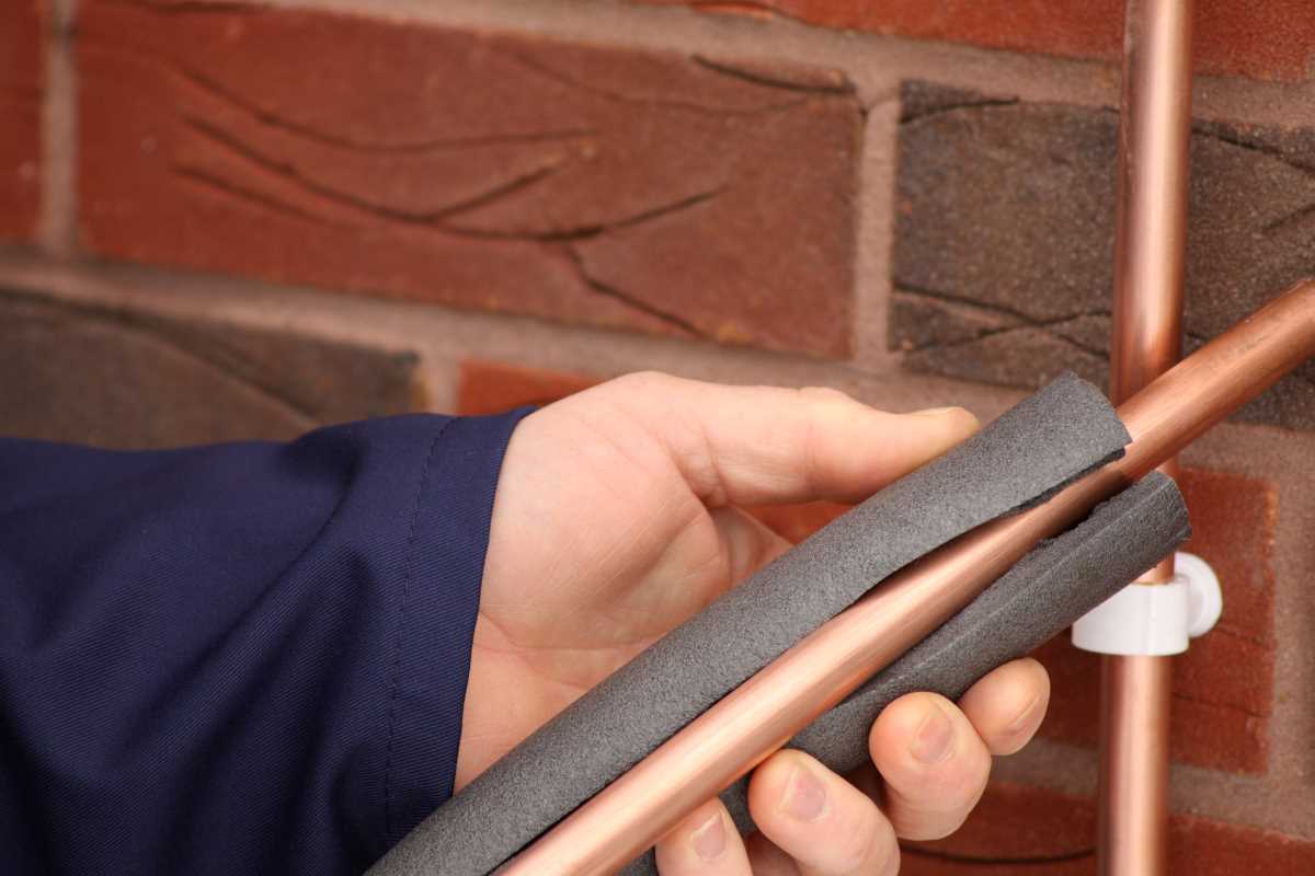 A hand holding a copper pipe with insulation