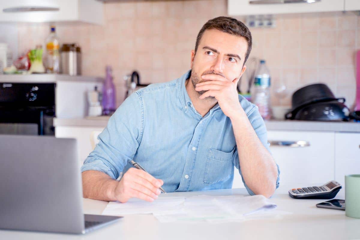 A man in his kitchen with papers and a laptop in front of him
