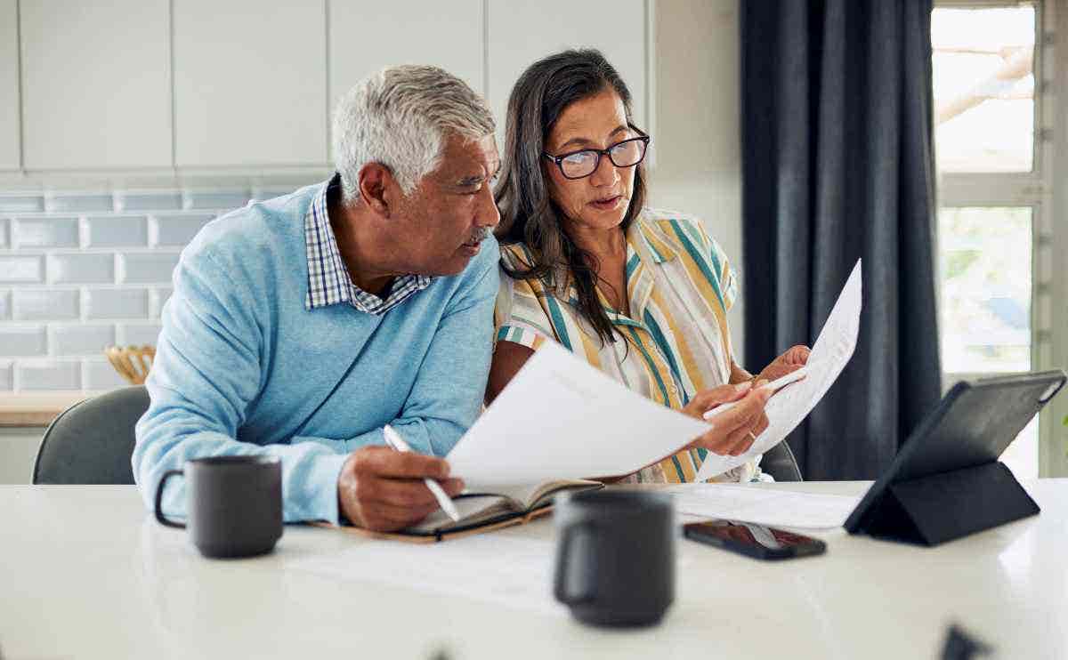 An older couple is sitting at their kitchen table reviewing financial documents.