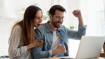 A man and a woman look at their computer and cheer