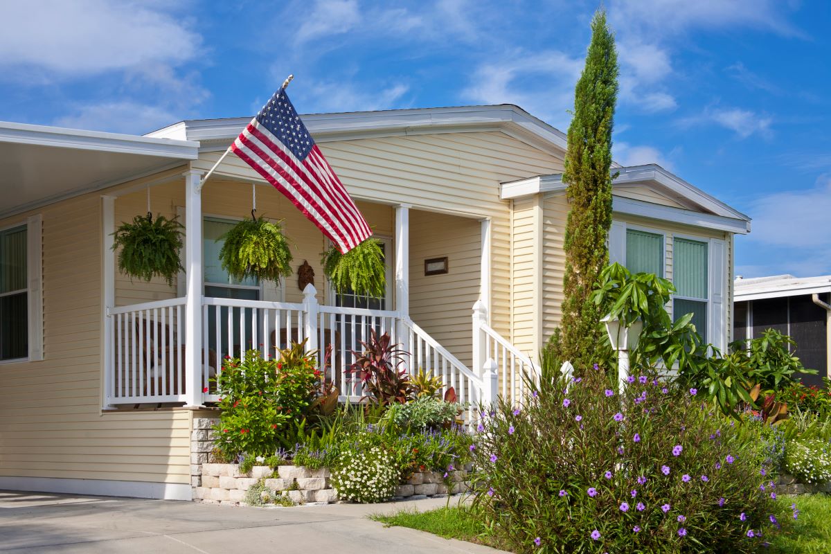 Mobile home with flower garden, front porch, and American flag