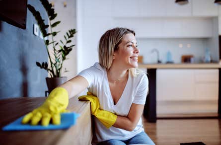 A woman wearing yellow gloves wiping down a shelf