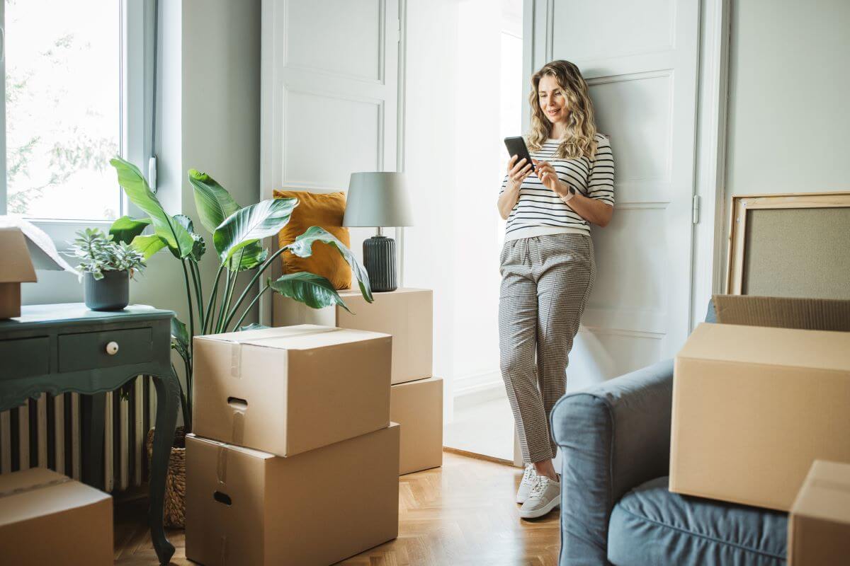 A woman in her new living ome surrounded by moving boxes and checking her smartpone