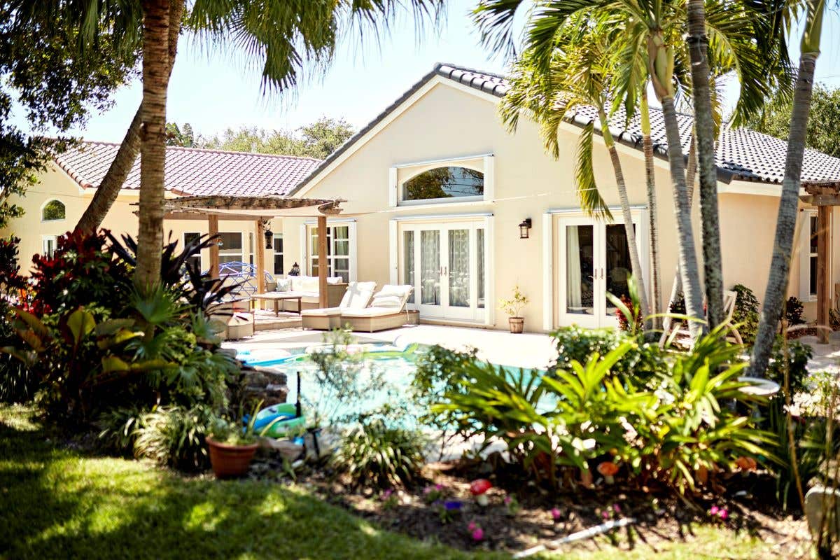 View from landscaped back yard of unoccupied patio with pergola, outdoor furniture, swimming pool, and modern home with tile roof