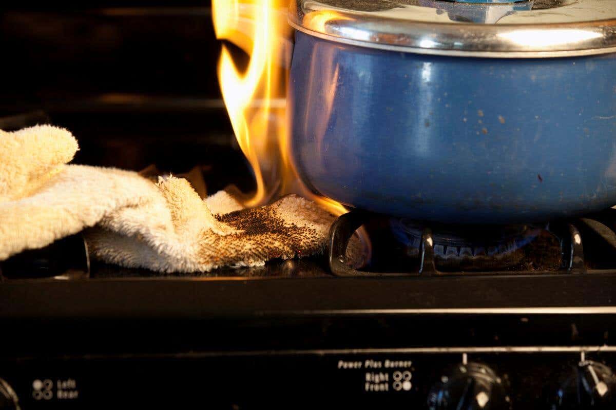 White towel catching fire on a stove top next to a blue pot