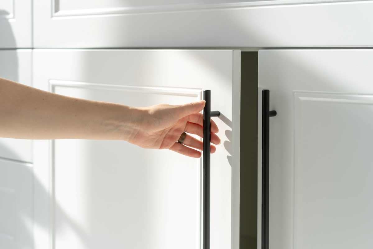 A hand opening a white cupboard