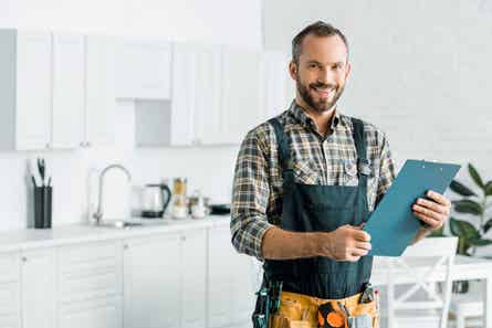 Smiling plumber standing in a kitchen, holding a clipboard and looking at the camera